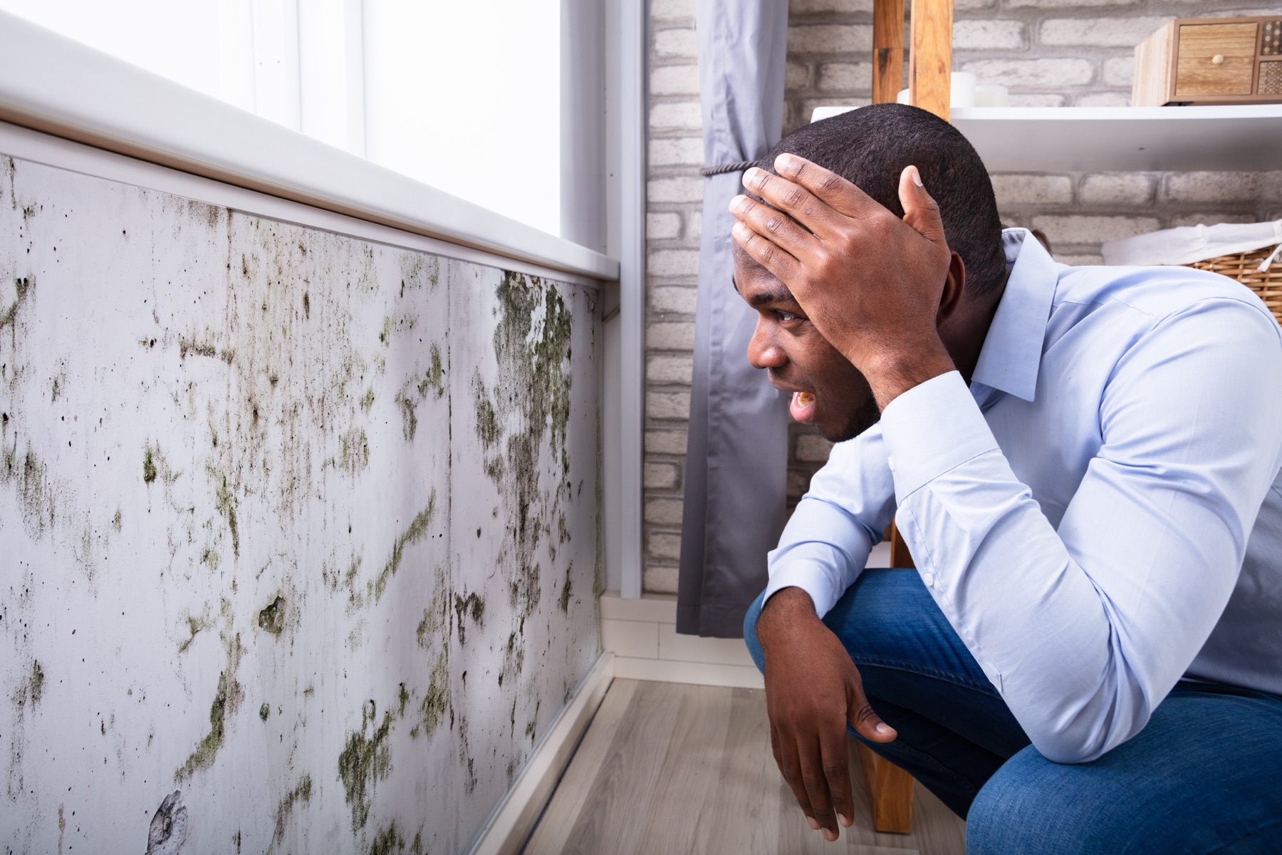 Man sitting with his head in his hand in front of a mold-covered interior wall